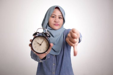 Başörtüsü takan genç Asyalı Müslüman kadın saat gösteriyor. Sinirli, hayal kırıklığına uğramış yüz ifadesi var. Beyazda izole edilmiş