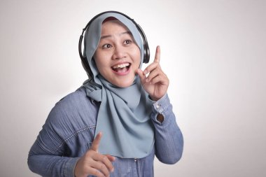 Güzel Asyalı Müslüman bir kadının portresi tesettür takıyor, kulaklıkla müzik dinliyor, dans ediyor.
