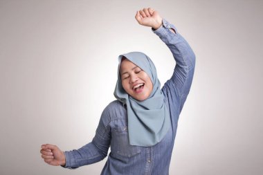 Türban lı komik bir Asyalı müslüman kadının portresi mutlu bir şekilde dans ederek iyi haber zaferini kutlayan başarı jestini kutluyor, beyaza izole pozitif heyecanlı duygular gülümsüyor