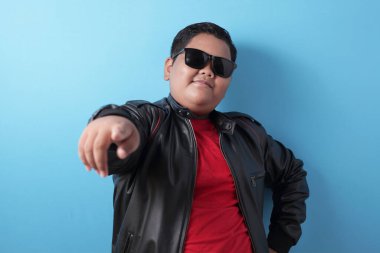 Şişko, zengin Asyalı çocuk kameraya gururla gülümsüyor. Siyah deri ceket ve güneş gözlüğü takan çocuk.