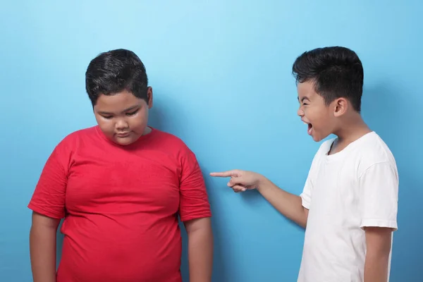 Asian boy bullying mocking other boy, fat boy get bullied at school, against blue background