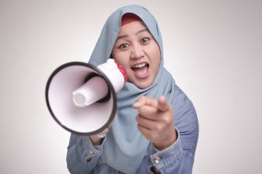 Genç Asyalı Müslüman kadın tesettür takmış megafonla bağırıyor ve kamerayı işaret ediyor. Lider destekçi ya da protestocu konsepti. Vücut portresini kapat