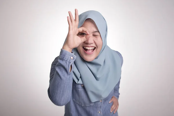 カメラを向けるアジア系イスラム教徒の女性の肖像画は 白に隔離されたOkサインジェスチャーを示しながら 彼女の指を見ているか 目を通して笑っています — ストック写真