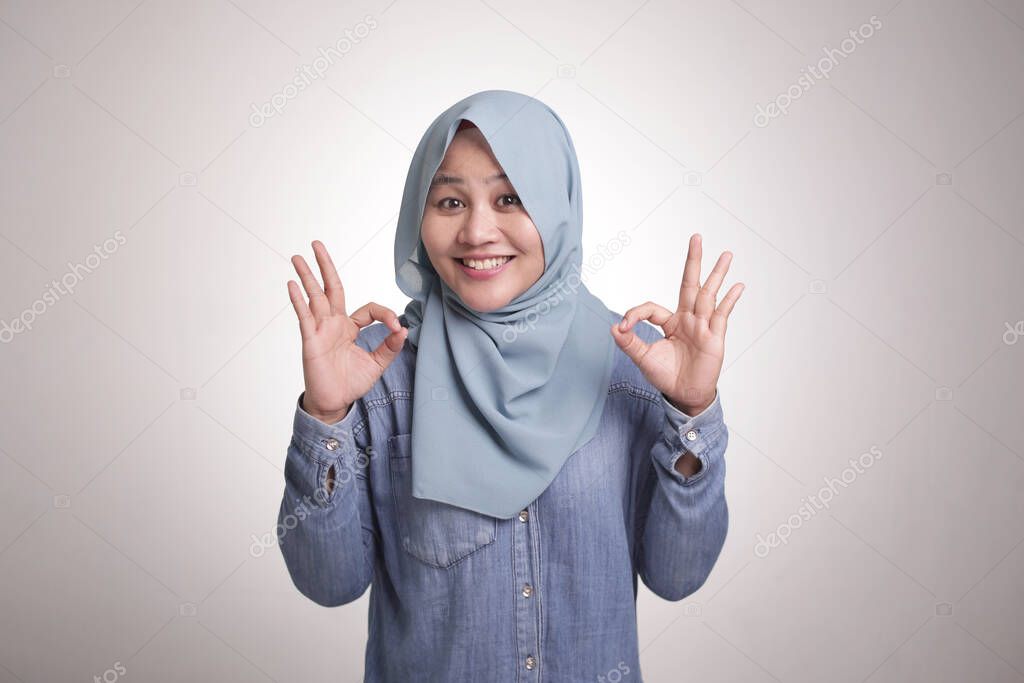 Portrait of beautiful Asian muslim woman smiling while making delicious hand gesture with her fingers, isolated on white