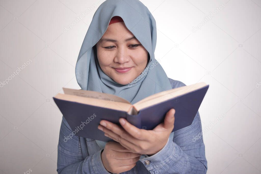 Portrait of young muslim business woman wearing hijab reading book and smiling, educational or leisure activity concept