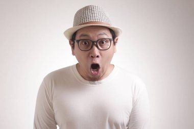 Beyaz gömlekli komik Asyalı genç bir adamın portresi, beyaz arka planda dururken ağzı açık, şok olmuş veya şaşırmış bir ifade sergiliyor.