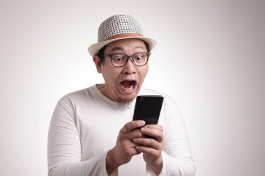 Çekici Asyalı genç adam telefonunda mesajlaşan mesajları okuyor, şaşırmış yüz ifadesi.