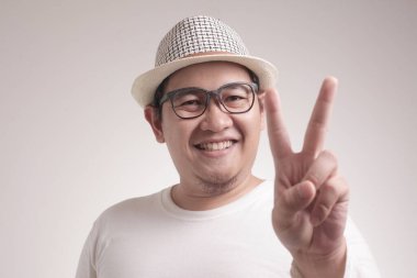 İyi görünümlü genç Asyalı adam Portresi beyaz duvara karşı parmağıyla iki numara veya barış işareti jest gösterir