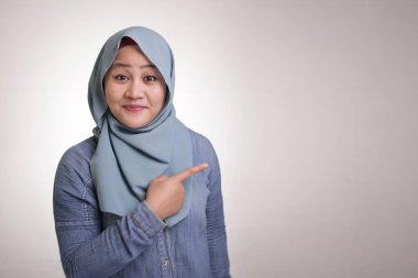 Asyalı Genç mutlu Müslüman kadın portre gülümseyen ve onun tarafında bir şey sunma işaret, kopya alanı ile