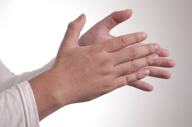 Beyaz tişörtlü genç Asyalı adam, mutlu bir alkış hareketi. Gri arka planda, yarım vücut portresi üzerinde.