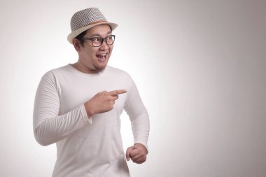 Küçük Asya giyen beyaz gömlek gülümseyen, gösterilen ve bir şey kopya alanı ile beyaz duvara onun tarafında işaret eden adamım. Vücut portre kadar kapatın