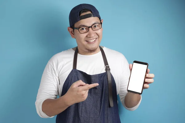 Portrait of Asian male chef or waiter looks happy and proud showing empty copy space smart phone, presenting blank phone template, copy space meal menu concept