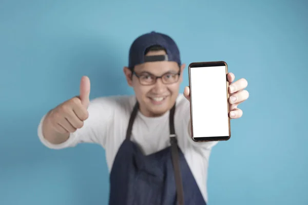 Portrait of Asian male chef or waiter looks happy and proud showing empty copy space smart phone, presenting blank phone template, copy space meal menu concept