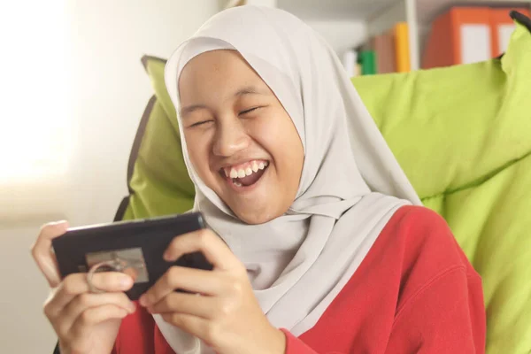 かわいいですアジアのイスラム教徒の十代の女の子のポートレート携帯電話でオンラインゲームをプレイヒジャーブを身に着けています 若い女の子幸せと興奮します — ストック写真