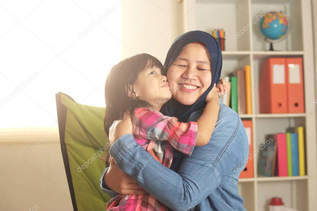 Muslim mother wearing hijab smiling while playing with her baby girl, mom and daughter love each other, happy single parent