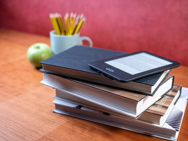 stacked classic books and an ebook with pens and apple