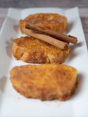 Beyaz tabakta tarçınlı ve hafif arka planlı üç Fransız tostu.