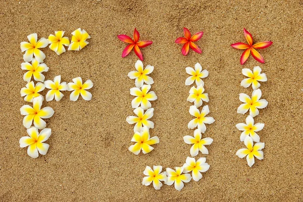 Wort Fiji, geschrieben an einem Strand mit Plumeria-Blumen — Stockfoto