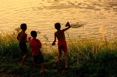 VANG VIENG, LAOS - NOVEMBER 25: Unidentified boy throw rocks in Nam Song River at sunset on November 25, 2011 in Vang Vieng, Laos. Vang Vieng is a tourist-oriented town in Vientiane Province.
