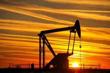 Gün batımında petrol sahasında siluetli pompa krikosu