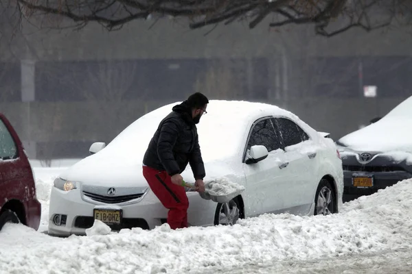 El hombre desentierra el coche con la pala durante la tormenta de nieve — Foto de Stock