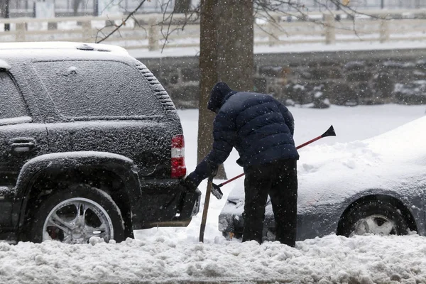 Człowiek czyści samochód z pędzla podczas burzy śnieżnej — Zdjęcie stockowe