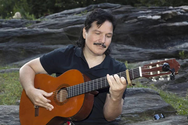 Homem hispânico sentado no parque tocando guitarra — Fotografia de Stock