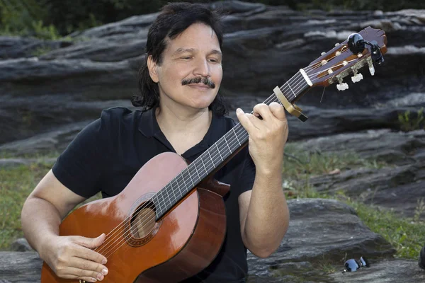 Hombre hispano sentado en el parque tocando la guitarra — Foto de Stock