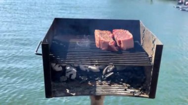 Delicious juicy beef meat steaks cooking on the grill. Flames coming from underneath the meat that is being cooked.Beautiful Bay on a background.