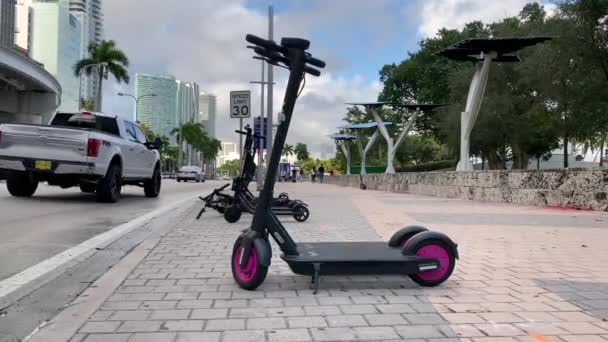 Scooters elétricos sendo estacionados em um dia ensolarado na calçada no centro da cidade de Miami. Transporte elétrico para estação de aluguel em Downtown Miami, Bayside Market . — Vídeo de Stock