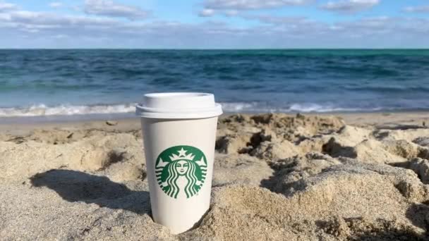 A Starbucks coffee on the sandy beach in Miami, Florida, USA. Starbucks Corporation is an American coffee company and coffeehouse chain. — 비디오