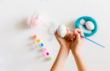 Çocuğun elleri paskalya yumurtalarını renklerle boyuyor ve açık arkaplanda fırçalıyorlar. Paskalya, bayramlar, gelenekler ve insanlar