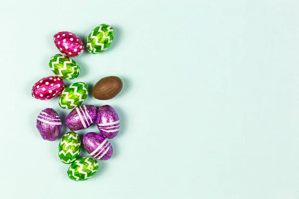 Coloridos huevos de Pascua de chocolate sobre fondo azul. Los huevos pequeños de chocolate en la laminilla. Dulce de Pascua tradicional. Copiar espacio — Foto de Stock