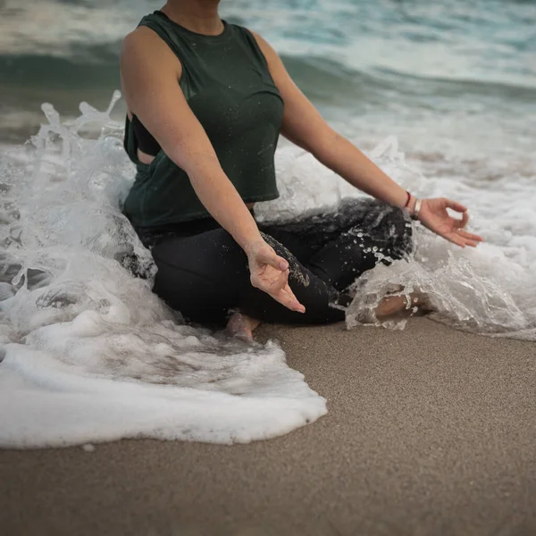 在海洋里做瑜伽的年轻女人，波浪覆盖着她。穿着运动服的迷人女人在户外放松一下。保健人员概念。复制空间 — 图库照片