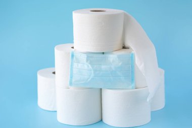  Tuvalet kağıtları istiflenmiş, mavi arka planda ilaç maskesi. Coronavirus COVID-19 karantinasına bağlı tuvalet kağıdı krizi. Boşluğu kopyala