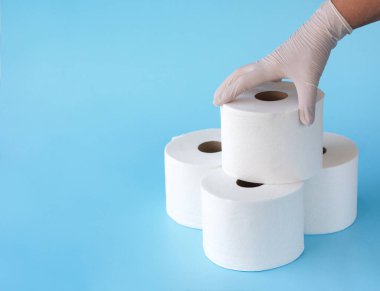 Tıbbi eldivenleri teslim edin. Mavi arka plandaki tuvalet kağıdı kulesinden tuvalet kağıdı rulosu alın. Coronavirus COVID-19 karantinasına bağlı tuvalet kağıdı krizi..