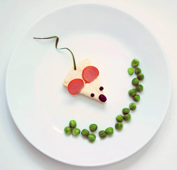 Little mouse from food. Funny food creative idea for breakfast. Beautiful mouse from sausage cheese greens peas on the white plate.