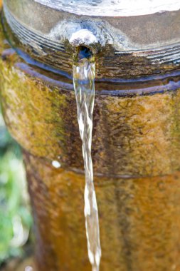 Eski ve paslı bir borunun içinde bir delikten su akışı