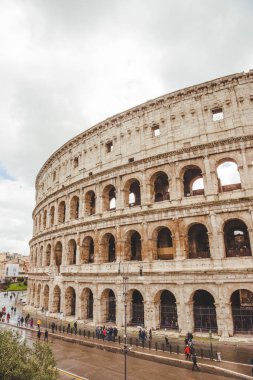 ROME, ITALY - 10 MARCH 2018: Colosseum ruins with tourists passing by on cloudy day clipart
