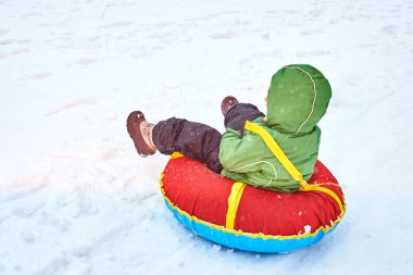 Küçük çocuk kışın kızakla kayıyor. Çocuk bir borunun üzerinde dağdan aşağı kayıyor.