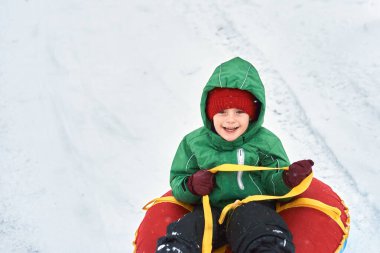 Küçük çocuk kışın kızakla kayıyor. Çocuk bir borunun üzerinde dağdan aşağı kayıyor.