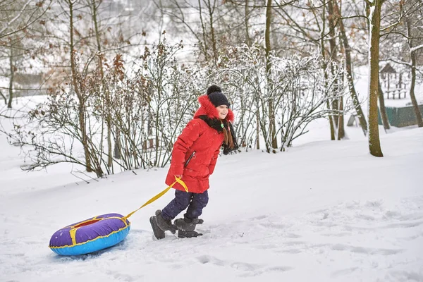 Holčička sjíždí z kopce na saních. dítě v zimním tubingu — Stock fotografie