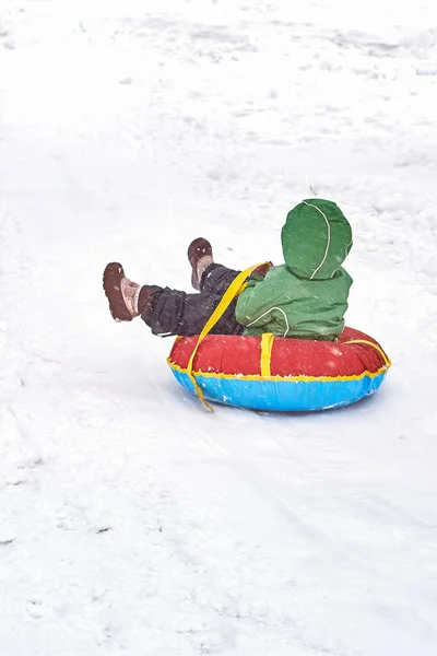 Malý chlapec sáňkaří v zimě. dítě sklouzne z hory na trubce — Stock fotografie