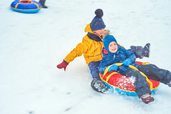 Malý chlapec sáňkaří v zimě. dítě sklouzne z hory na trubce — Stock fotografie