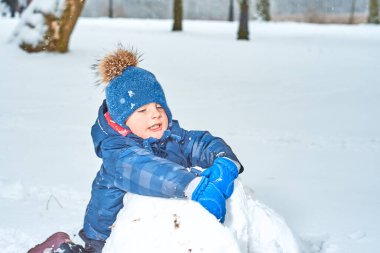Şapkalı ve eldivenli küçük çocuk kışın kardan adam yapar.