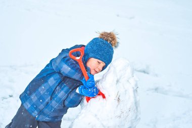 Şapkalı ve eldivenli küçük çocuk kışın kardan adam yapar.