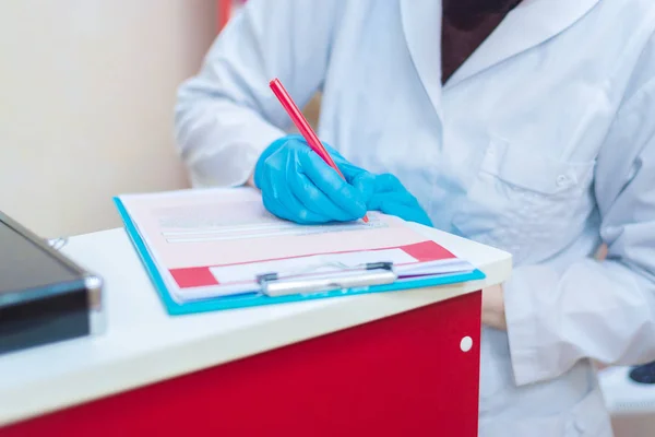 Mavi lastik eldivenli doktor bir anket ve hasta verisi dolduruyor.