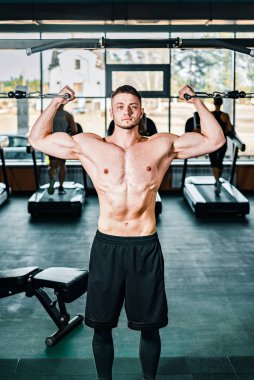 Tişörtsüz kaslı sporcu spor salonunda antrenman yapıyor. Fiziksel olarak iyi durumda çıplak gövdeli bir adam.