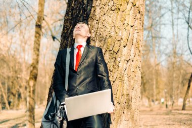 Ağacın yanında yorgun bir işadamı. Serbest çalışan güneşte dinlenir ve sevinir.