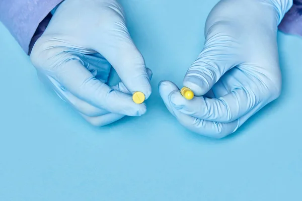 doctor holds yellow pills in his hands. medical worker in gloves. pharmacology. blue background